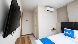 Quarto de hotel com televisão de tela plana na parede, cama com travesseiro azul e unidade de ar condicionado na parede.
