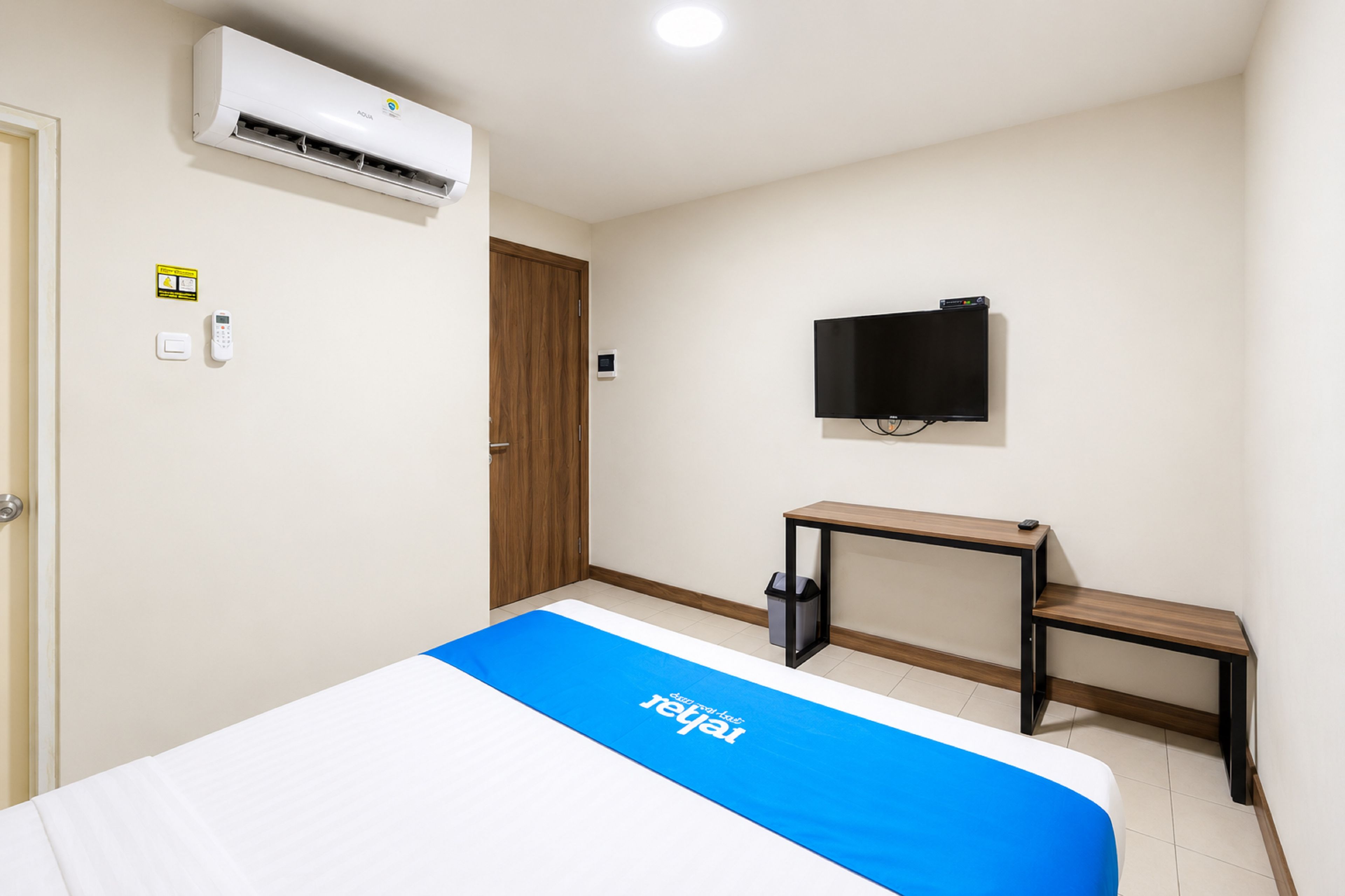 Habitación de hotel con cama, unidad de aire acondicionado, televisor, escritorio y cubo de basura.