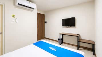 Habitación de hotel con cama, unidad de aire acondicionado, televisor, escritorio y cubo de basura.