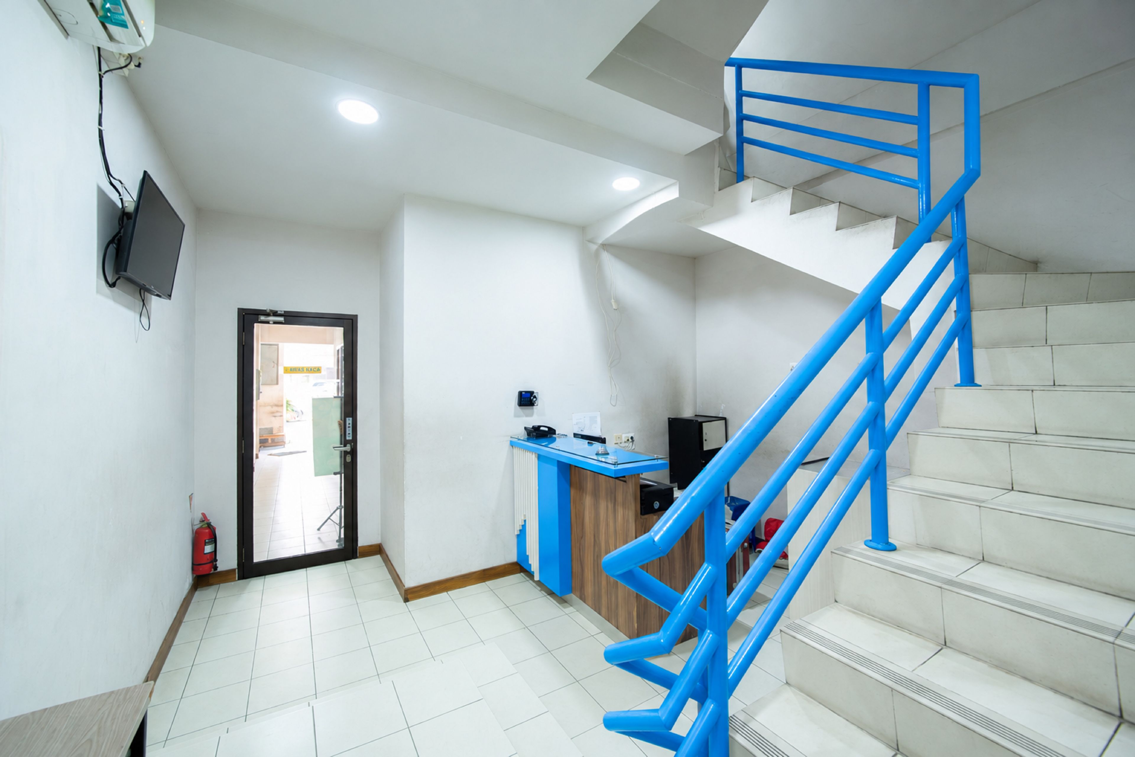 A staircase with blue railings leading to an upper floor, a reception desk, and a fire extinguisher on the floor.
