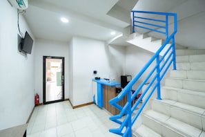 Una escalera con barandillas azules que lleva a un piso superior, un mostrador de recepción y un extintor en el suelo.