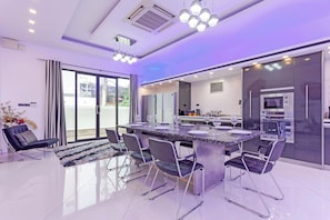 A modern kitchen with a central island, stainless steel appliances, and a dining area with a glass table and chairs. - Pratumnak Hill PoolVilla 4BR Luxury(PH2) (Banglamung)