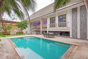 Un espace piscine moderne doté d’une piscine à eau claire, d’un espace salon extérieur et d’une structure à plusieurs niveaux avec des balcons.