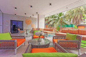 Un espace de détente moderne, avec des meubles en osier, une table basse en verre et une vue sur des palmiers.