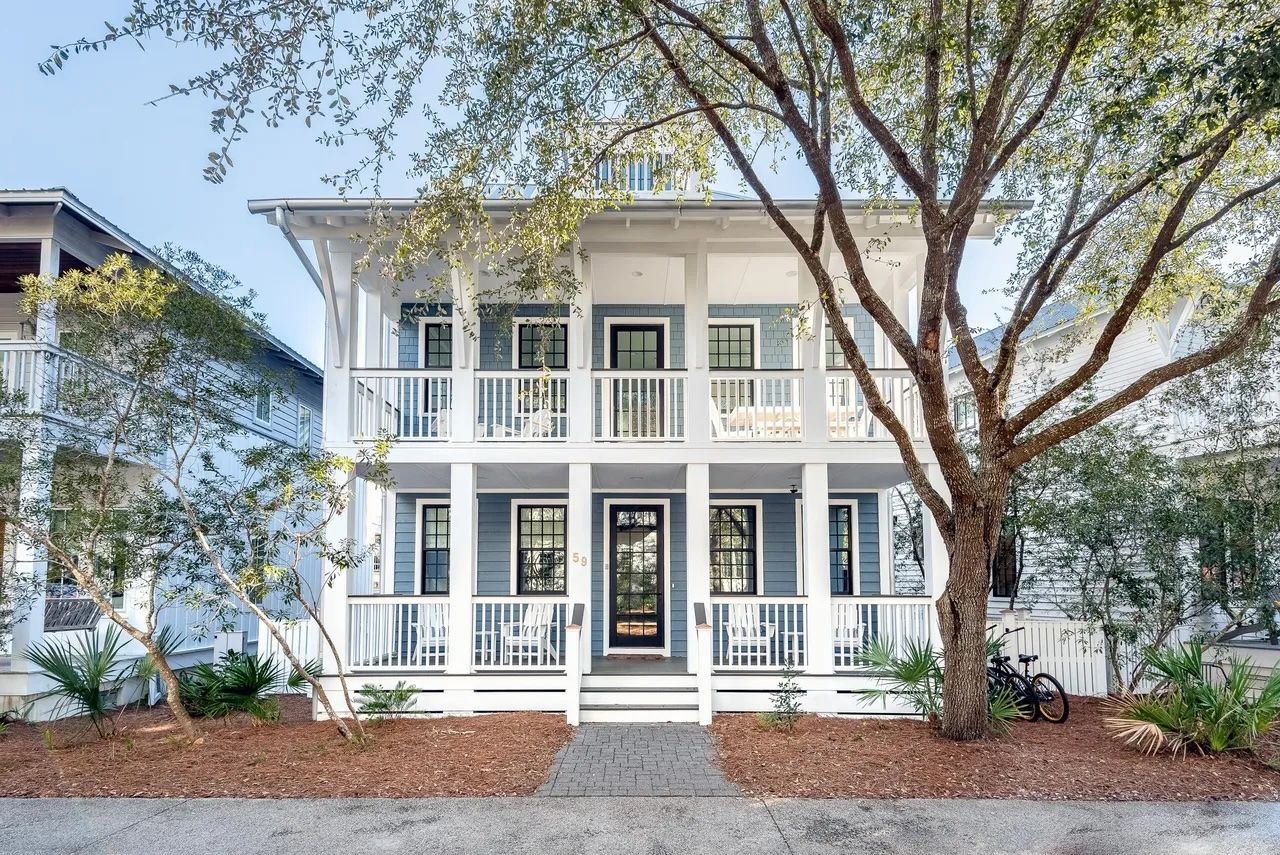 A two-story house with a porch, a tree in front, and a bicycle parked to the side.