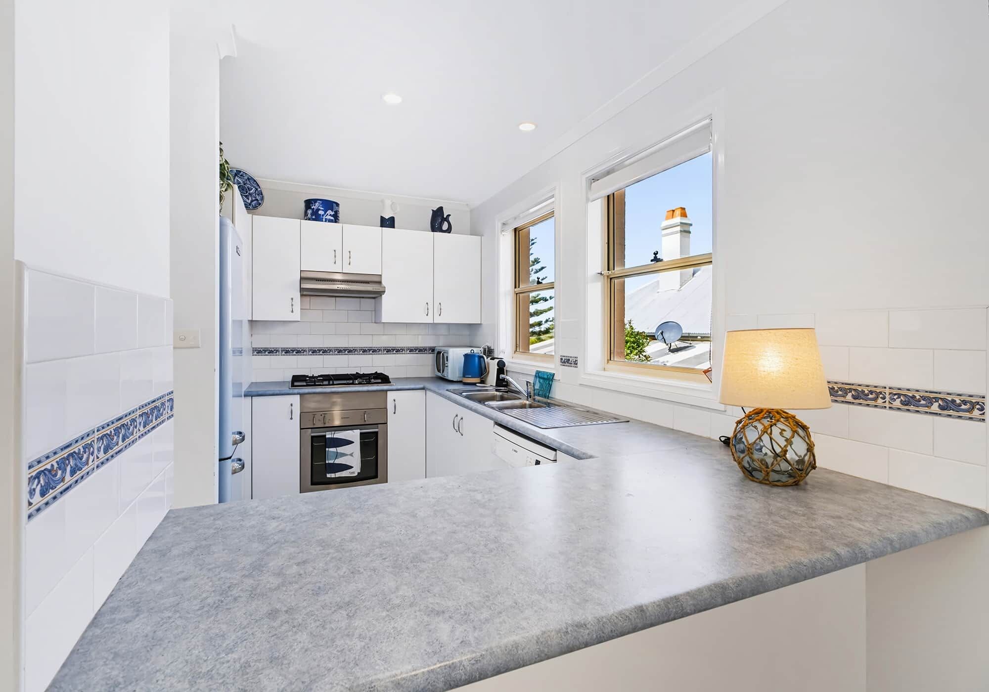 A modern kitchen with white cabinets, a built-in oven, a sink, and a window with a view of the outside.