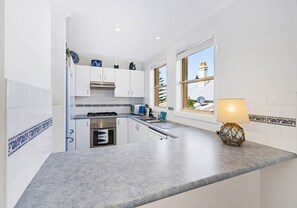 A modern kitchen with white cabinets, a built-in oven, a sink, and a window with a view of the outside. - Ocean Tracks - 2/1 Eddy Street Kiama (Kiama)
