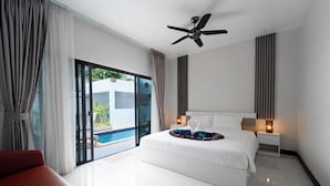 A modern hotel room with a large bed, a ceiling fan, a nightstand with lamps, and a view of a swimming pool. - Elyana Haven | Luxury 3BR Private Pool Villa in Rawai, Phuket (Tambon Rawai)