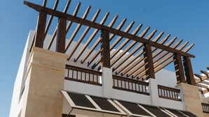 Een modern gebouw met een houten pergola, meerdere balkons en een heldere lucht.