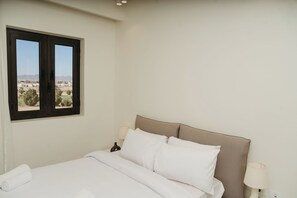 Un dormitorio con una cama, dos lámparas de noche, un ventanal con vistas y una lámpara de pared.