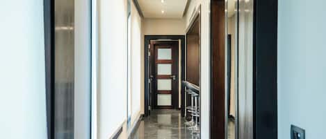 A modern hotel hallway with a marble floor, a wooden door at the end, and a bar area with stools.