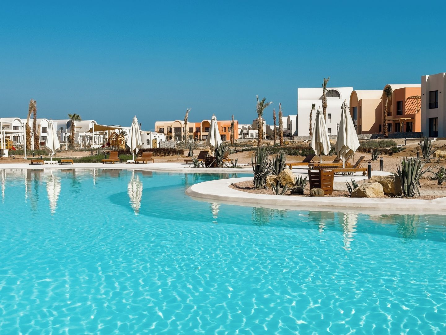 A resort pool area with lounge chairs and umbrellas, surrounded by resort buildings.