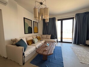 Een moderne woonkamer met een modulaire bank, een houten salontafel en een groot raam met gordijnen.