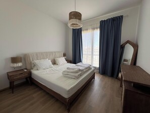 A hotel room with a bed, bedside table, lamp, and a view of the outdoors. - Kamaran 2BR • Luxurious Retreat (Hurghada)