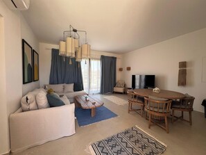 A modern living room with a sofa, coffee table, dining table, and TV. - Kamaran 2BR • Luxurious Retreat (Hurghada)