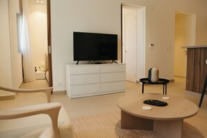 Ein modernes Wohnzimmer mit einem Flachbildfernseher auf einer weißen Kommode, einem runden Couchtisch mit Fernbedienungen und einer Holzsideboard.