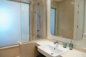 Un baño moderno con ducha envuelta en vidrio, un lavabo blanco y un espejo grande.