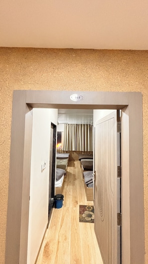 A corridor leading to a room with a bed, a small table, and a curtain. - The Grand Avantika Hotel and Resorts (Tarana)