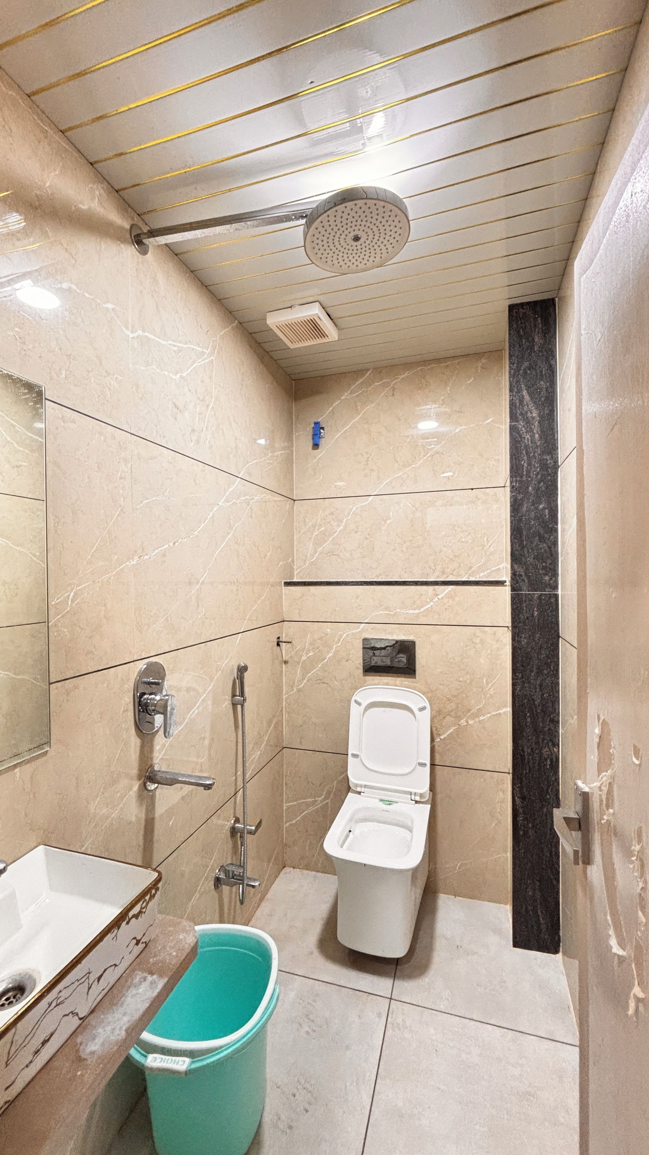 A bathroom with a toilet, a sink, a shower, and a bucket.