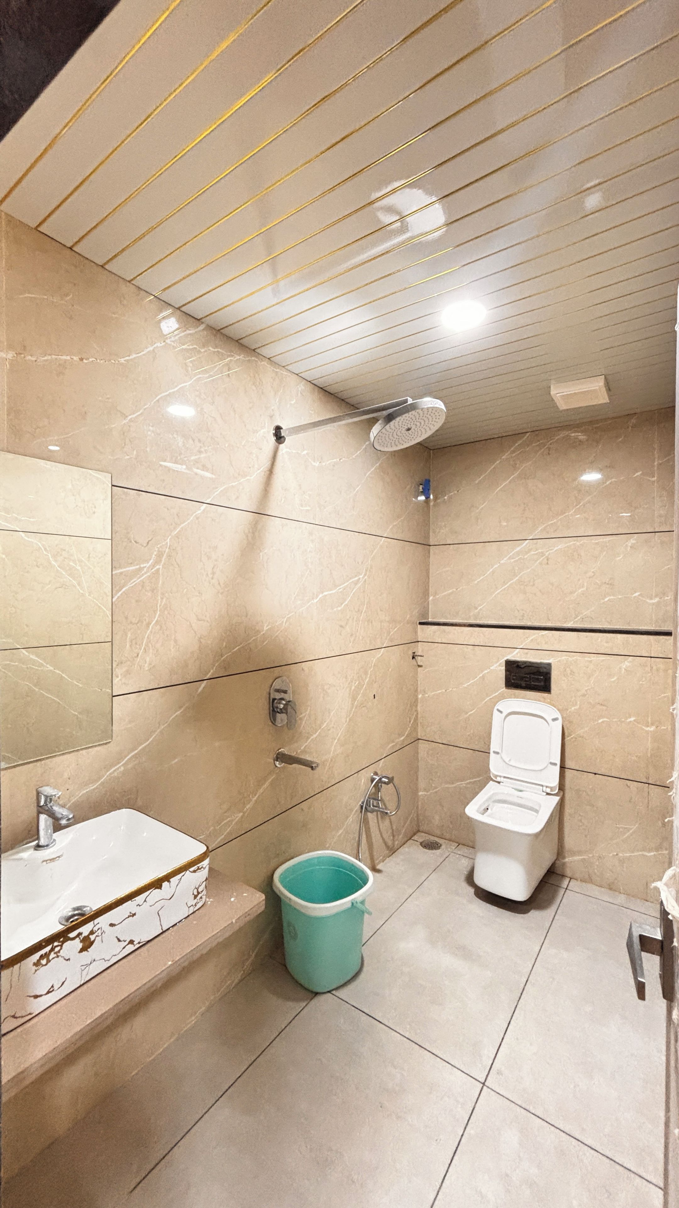 A bathroom with a shower, toilet, sink, and a bucket.