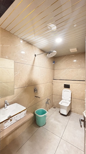 A bathroom with a shower, toilet, sink, and a bucket. - The Grand Avantika Hotel and Resorts (Tarana)