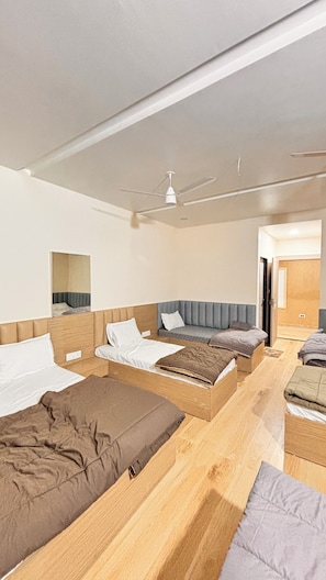 A hotel room with three beds, a ceiling fan, and a door leading to another room.