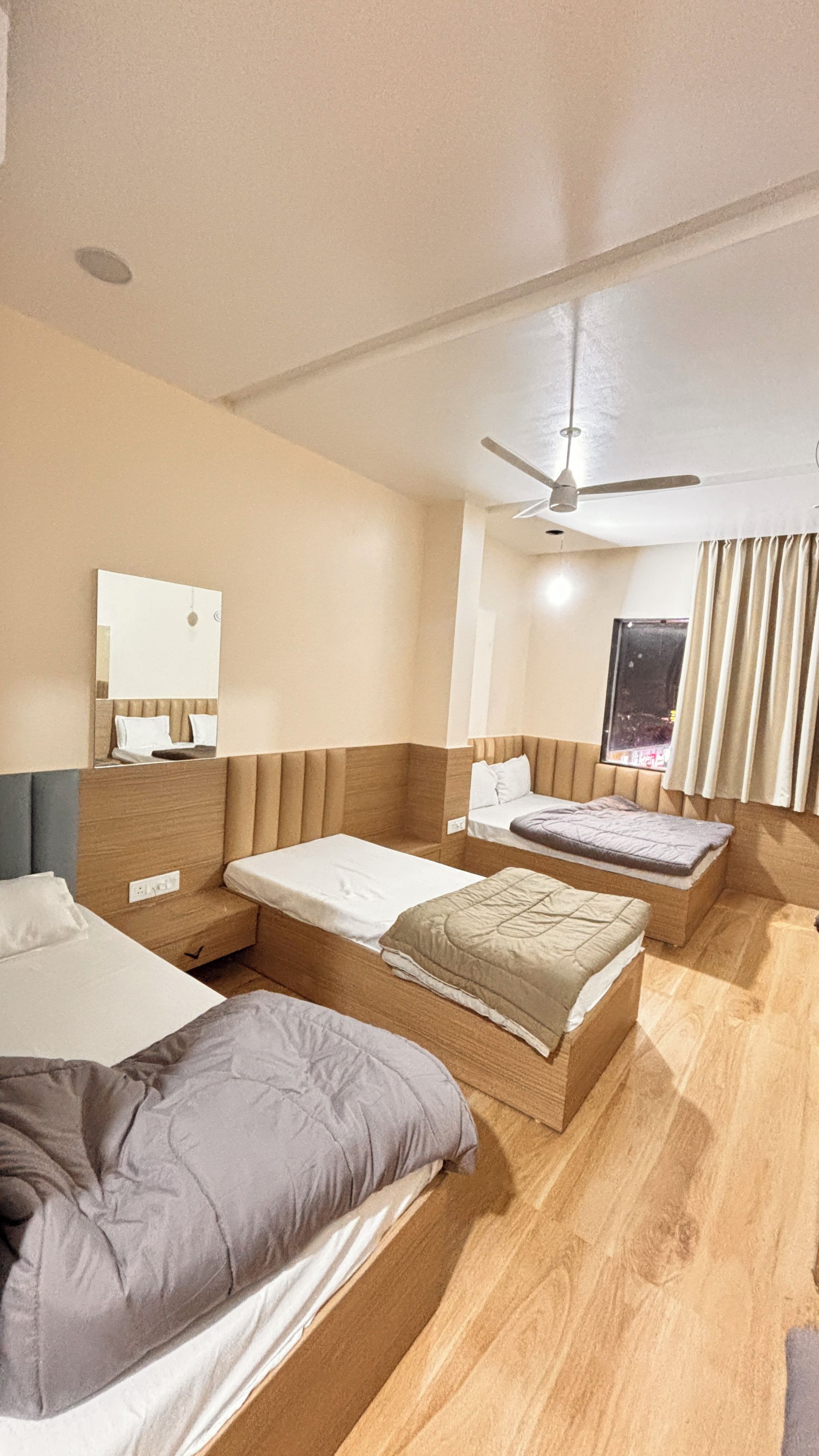 Ein Hotelzimmer mit zwei Betten, einem Deckenventilator, einem Fenster mit Vorhängen und einem Spiegel an der Wand.