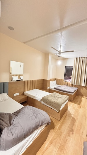A hotel room with two beds, a ceiling fan, a window with curtains, and a mirror on the wall. - The Grand Avantika Hotel and Resorts (Tarana)