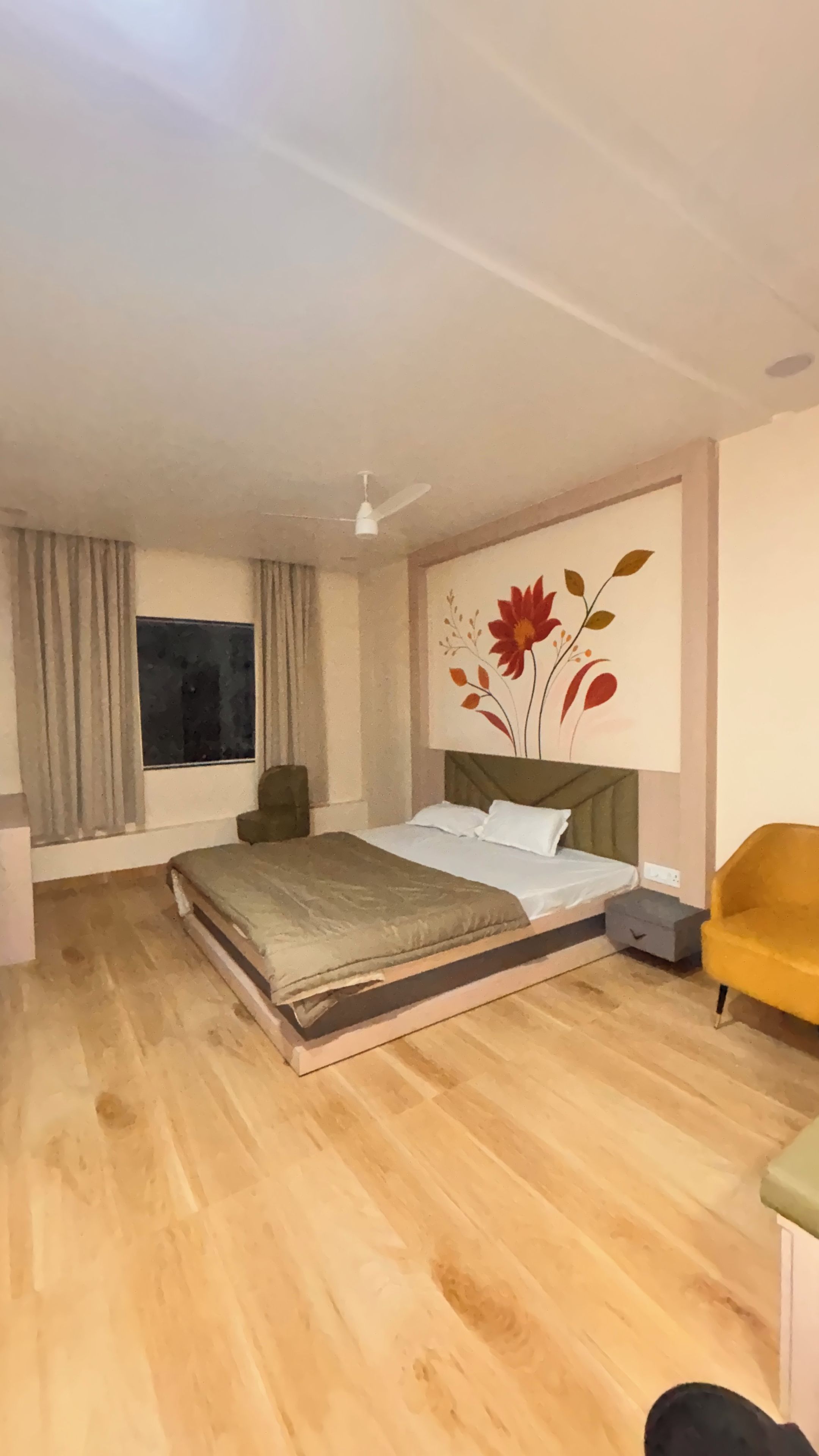 Un dormitorio con cama, mesita de noche, una silla, ventana con cortinas y ventilador de techo.