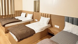 Habitación de hotel con tres camas individuales, un ventilador de techo y una ventana grande con cortinas.