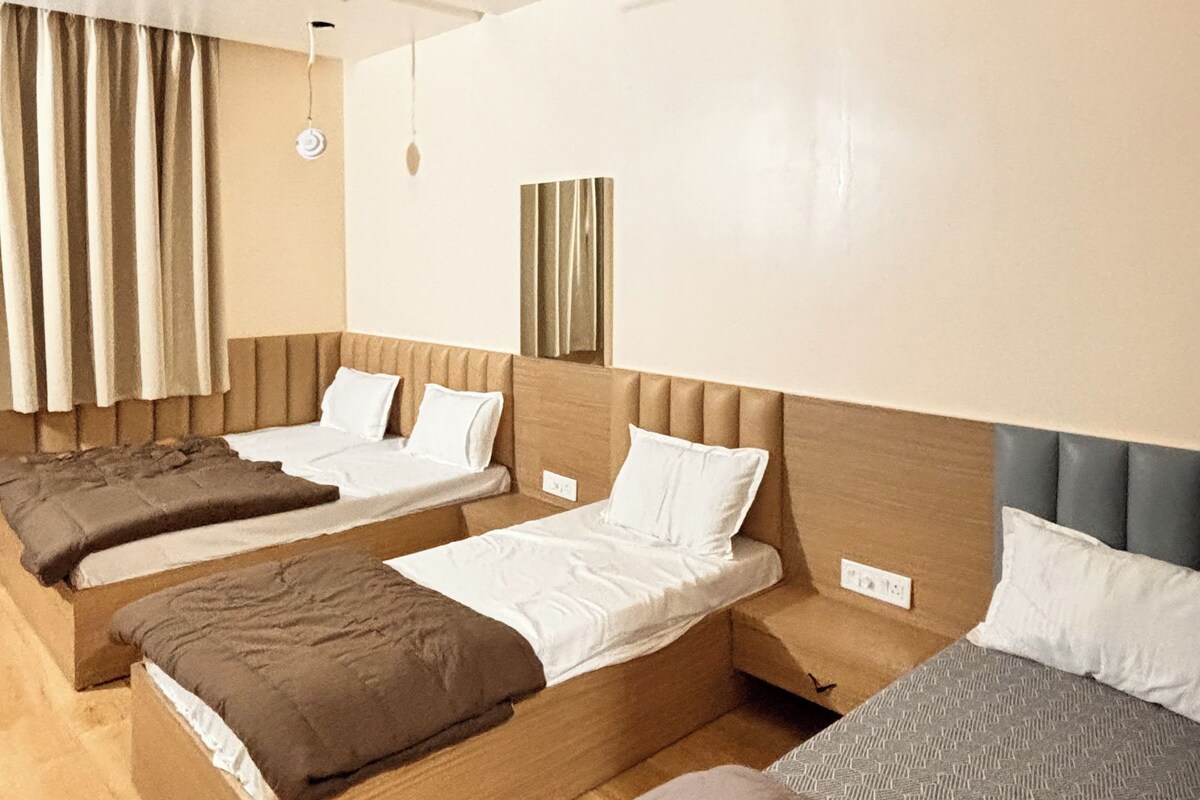Habitació d'hotel amb tres llits individuals, un ventilador de sostre i una finestra gran amb cortines.