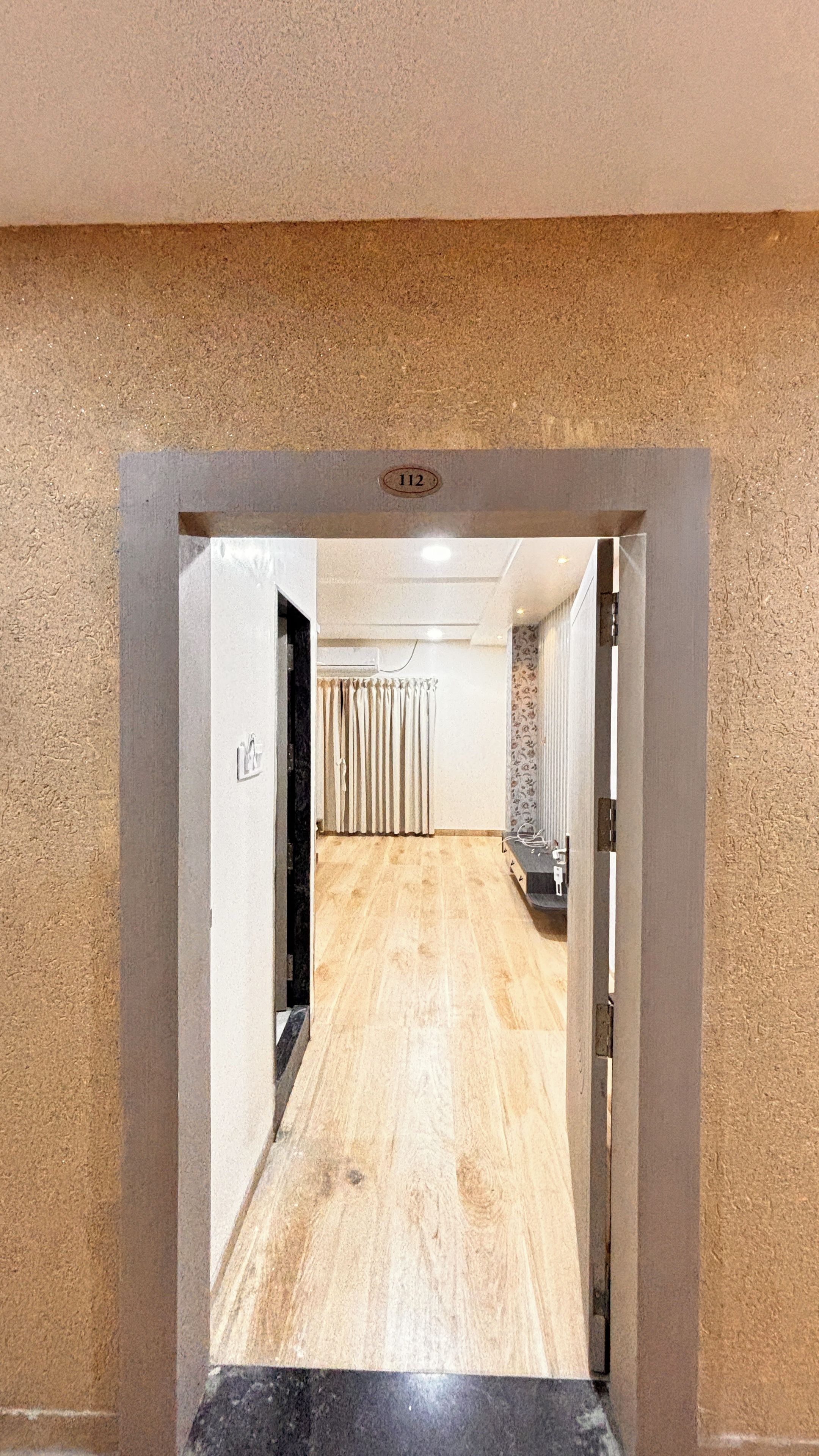 A corridor with a wooden floor, a door with a number plate, and a curtain.