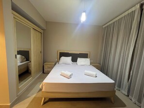 A hotel room with a large bed, a bedside table, a wardrobe, and a window with curtains. - Beachside Mangroovy 1BR (Red Sea)