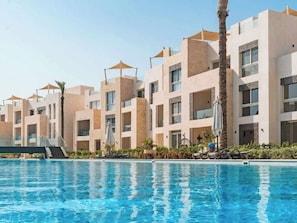 A hotel with a swimming pool, multiple balconies, and palm trees. - Beachside Mangroovy 1BR (Red Sea)