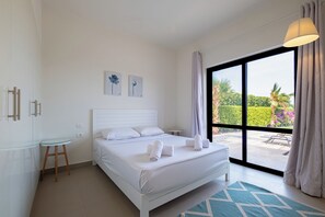 A modern bedroom with a large bed, a small side table, and a view of a garden through a sliding glass door. - Fanadir 3BR • Prime Sea View Villa (Hurghada 2)