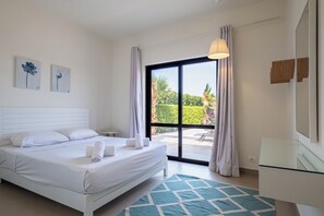 A hotel room with a bed, a small table, a mirror, and a view of the outdoors.