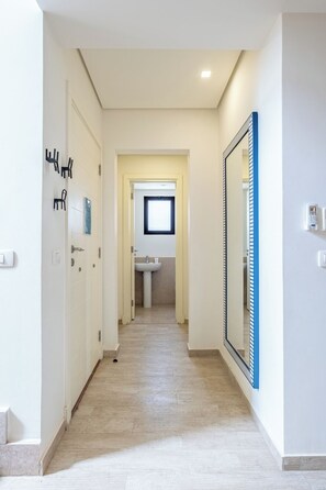A hallway with a light-colored tiled floor, a door with a keyhole, a wall-mounted security device, and a mirror reflecting part of the hallway. - Fanadir 3BR • Prime Sea View Villa (Hurghada 2)