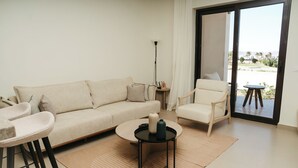 Een moderne woonkamer met een bank, fauteuil, salontafel en uitzicht door een glazen deur.
