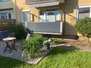 A residential building with a covered outdoor seating area, a small garden with a lawn and gravel path, and a wooden bench. - Holiday Apartment With 1 Bedroom (Goslar)
