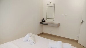 Hotellihuone, jossa on sänky, seinälle kiinnitetty peili, pieni hylly maljakolla ja ovi.
