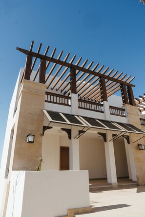 Ein modernes Gebäude mit einer Holz-Pergola, mehreren Balkonen und blauem Himmel.