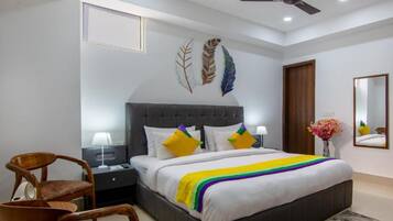 Une chambre avec un grand lit, deux tables de chevet, une chaise, un ventilateur de plafond et des œuvres d’art décoratives au mur.