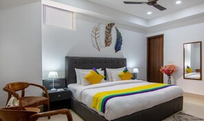 A bedroom with a large bed, two bedside tables, a chair, a ceiling fan, and decorative wall art. - Hotel Divine India Noida Sector 135 (Noida)
