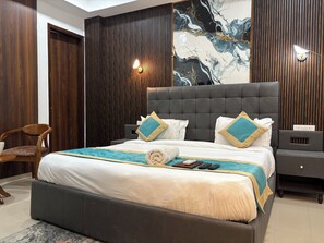 A modern bedroom with a large bed, a wooden wardrobe, a seating area, and a marble wall. - Hotel Divine India Noida Sector 135 (Noida)