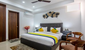 A bedroom with a bed, a ceiling fan, a decorative wall piece, and a nightstand with a lamp. - Hotel Divine India Noida Sector 135 (Noida)