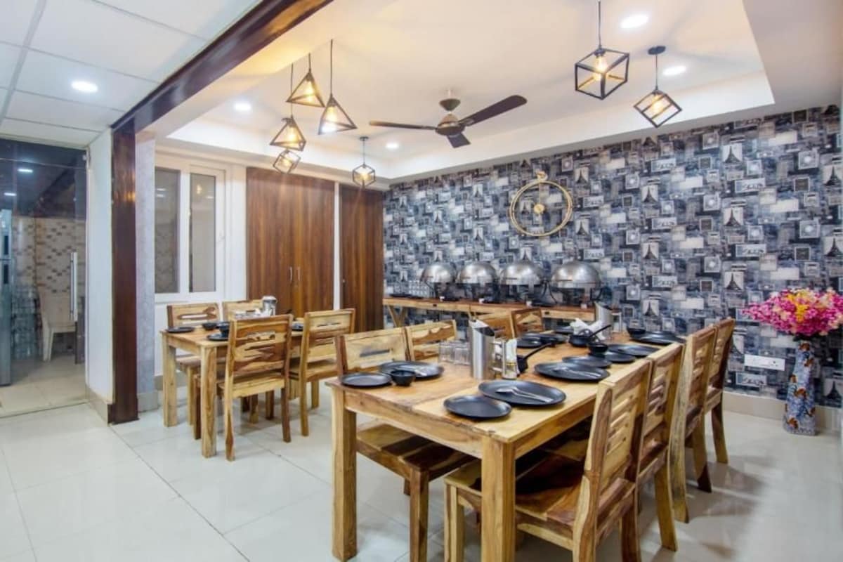 A dining area with wooden tables and chairs, pendant lights, and a patterned wall.