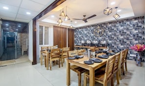 A dining area with wooden tables and chairs, pendant lights, and a patterned wall. - Hotel Divine India Noida Sector 135 (Noida)