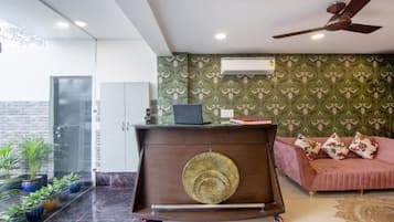 Un salon moderne avec un canapé, un mur décoratif, un ventilateur de plafond et un ordinateur portable posé sur une petite table.