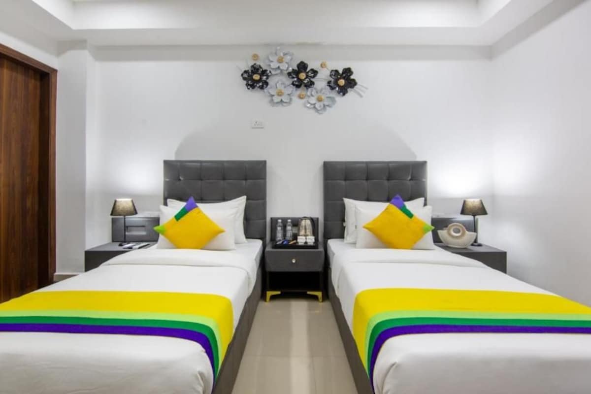 A hotel room with two beds, a nightstand with a lamp, and a decorative wall piece.