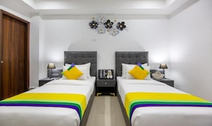A hotel room with two beds, a nightstand with a lamp, and a decorative wall piece. - Hotel Divine India Noida Sector 135 (Noida)